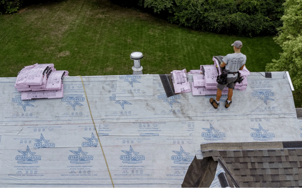 A man working on a roof replacing the shingles with part of the roof already done