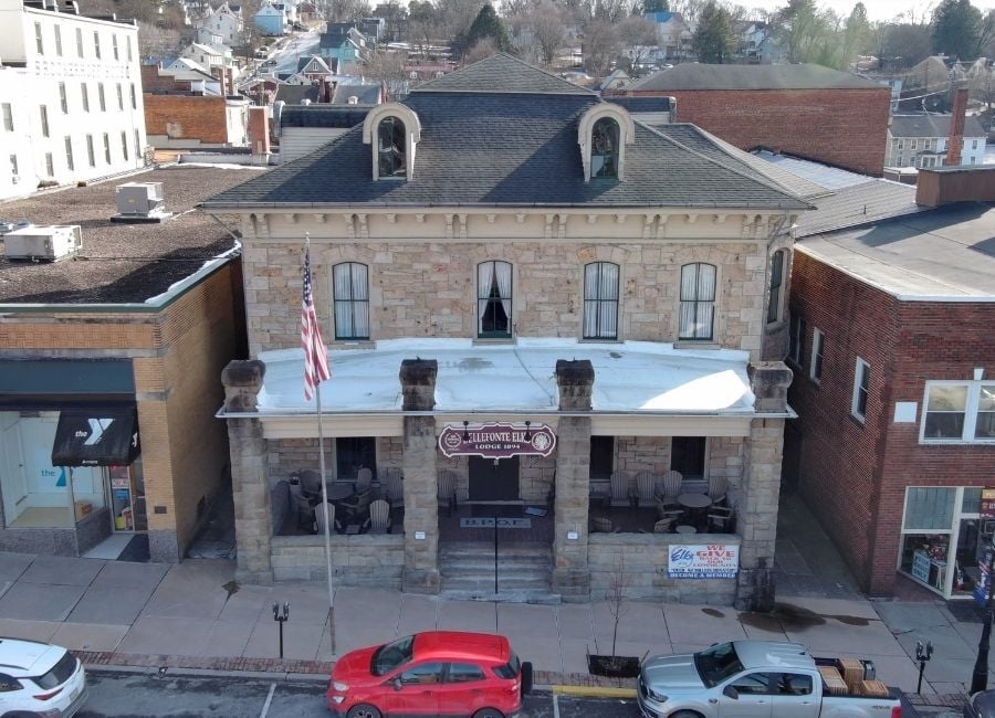Aerial view of a stone building with a dark hipped roof, arched dormers, and a snow-covered porch roof